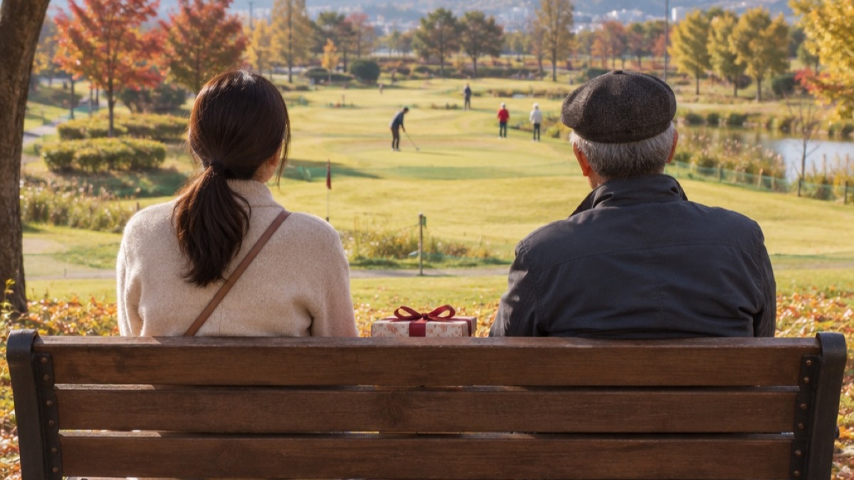 가을 파크골프장 옆 나무 벤치에 선물 상자를 사이에 두고 앉아 멀리 경기하는 사람들을 바라보는 딸과 아버지의 뒷모습